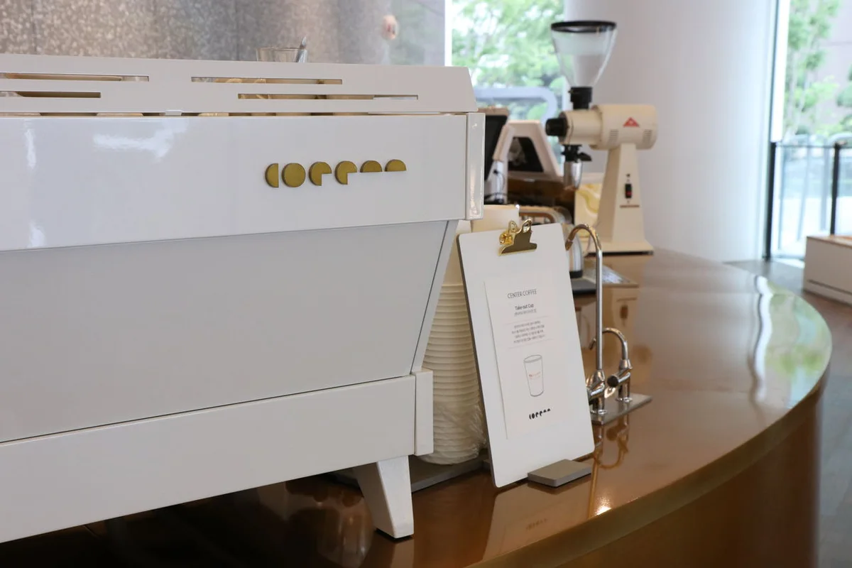 White espresso machine and grinder on a curved wooden counter at Center Coffee’s Samseong branch.