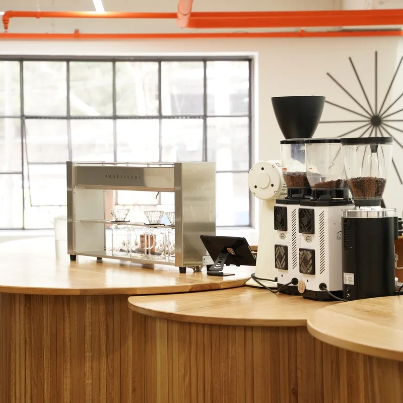 Curved wooden brew counter with white grinders and filter drippers at El Cafe’s Huam branch.
