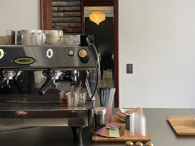 The espresso machine and wooden service counter at Lowkey Coffee Yeonhui, with a chandelier visible in the adjoining room.