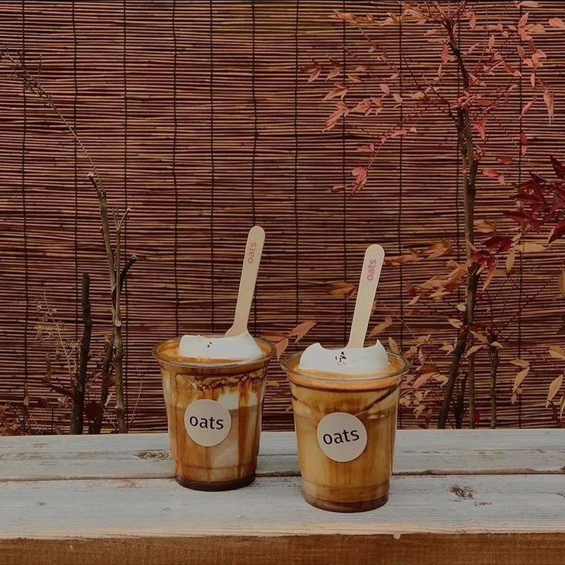 Two cream-topped coffees in Oats-branded cups against a bamboo blind at the Yongsan branch.