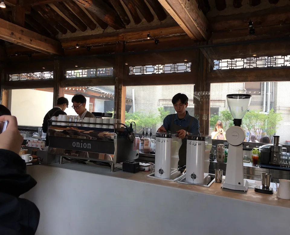 Baristas and a white espresso machine beneath timber beams at Onion Anguk