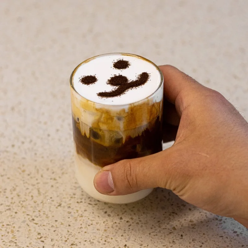 A hand holding up.side’s cream-topped coffee with a smiling face above the Seongsu café’s branded counter.